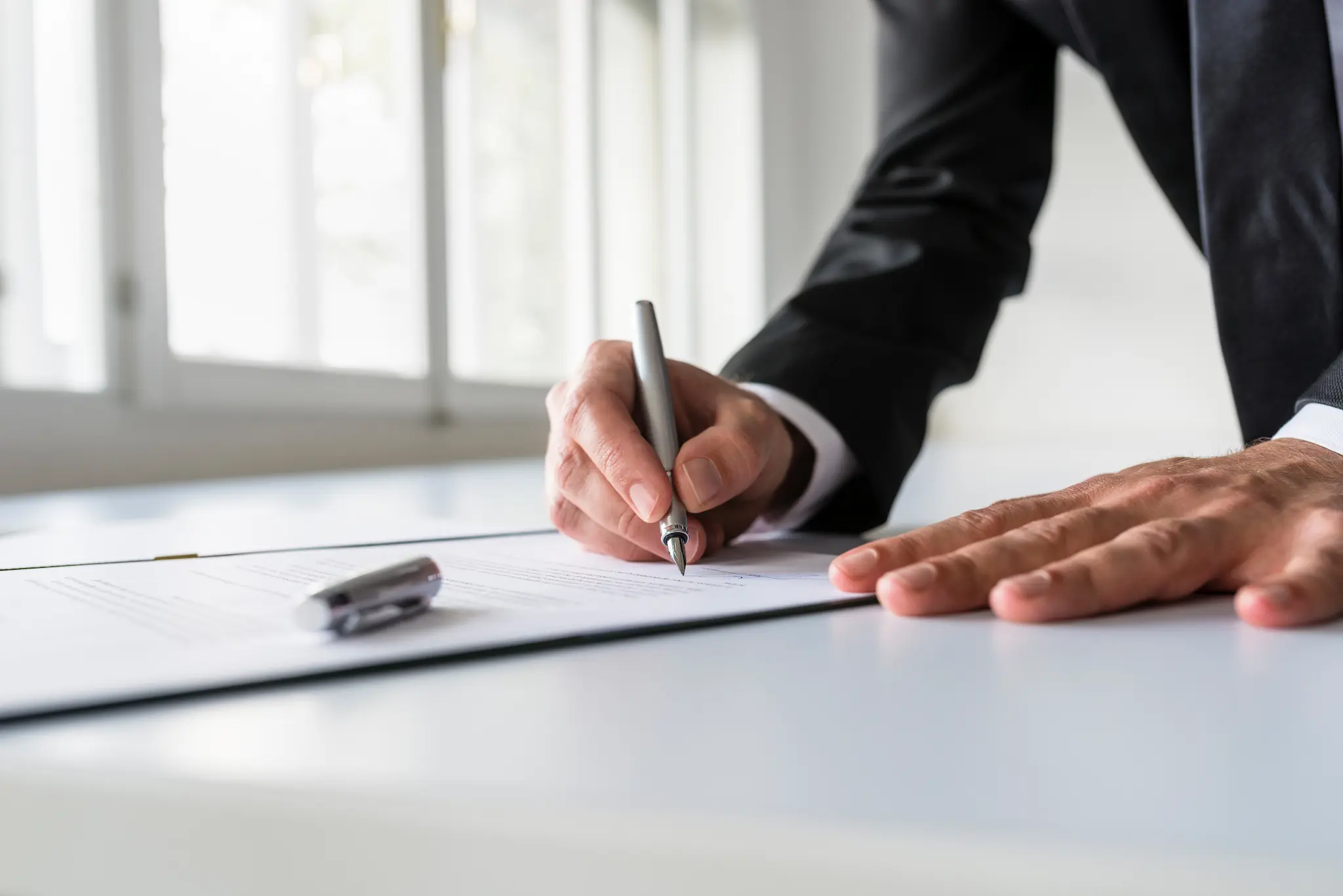 Primer plano de un hombre firmando un contrato en una oficina con bolígrafo plateado.