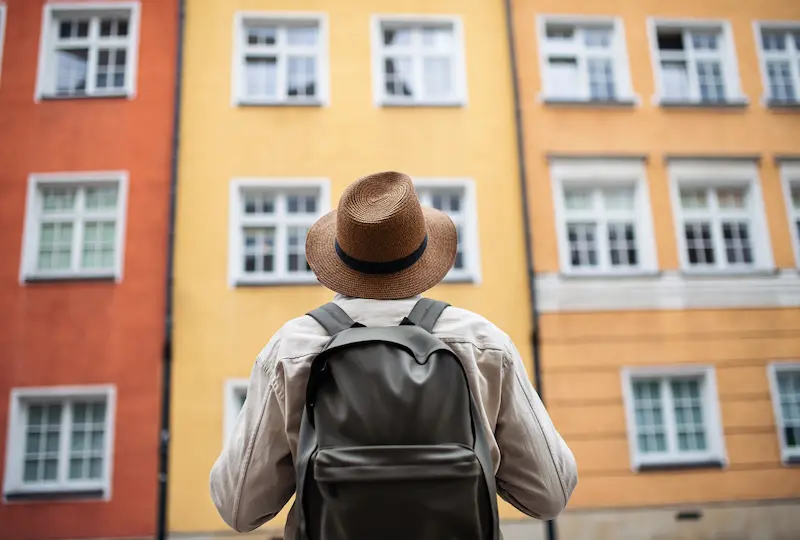 Persona con sombrero y mochila observando un edificio de colores, representando viviendas potencialmente destinadas al alquiler turístico.