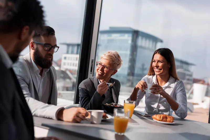 Grupo de personas desayunando en una reunión de trabajo junto a una ventana con vista urbana